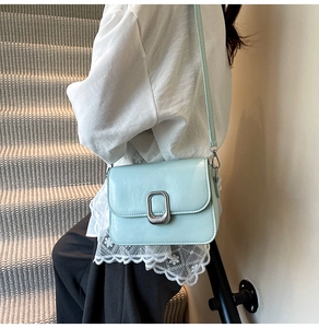 Mint green leather crossbody bag with silver buckle worn over a white lace blouse