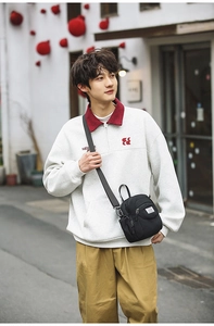 Detail of a black multi-pocket nylon crossbody bag worn with a white streetwear sweatshirt