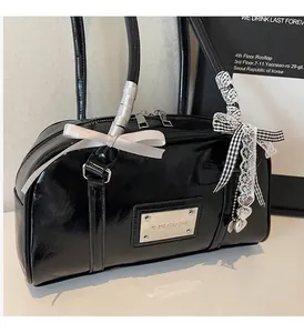 Detailed view of shiny black patent leather bag with silver logo plate and bow charm