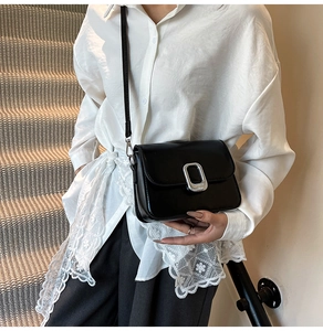 Detail of a minimalist black leather square crossbody bag with a silver metal buckle