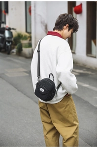 Outdoor street style view of a black mini crossbody bag with adjustable strap and logo