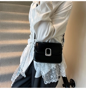 Detail of a chic black crossbody bag with silver buckle worn by a model on stairs
