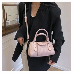 Detail of pink woven cylinder bag with leather logo tag and circular handle on a model