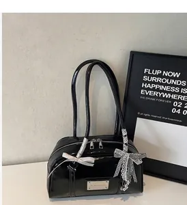 Detail of black glossy shoulder bag featuring dual zippers and decorative bow charms