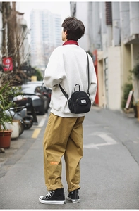 Detailed outdoor view of a compact black nylon messenger bag with white square label