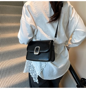 Detail of glossy black PU leather crossbody bag with silver buckle worn by a model