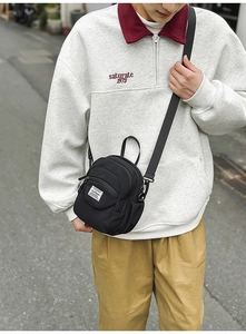 Close-up of a versatile black nylon mini crossbody bag worn by a model in a city street