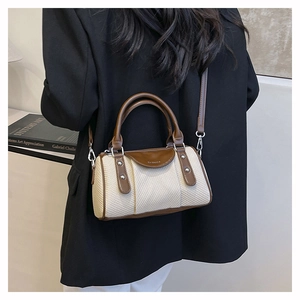 Detail of Boston-style woven crossbody bag with brown leather handles on a black blazer