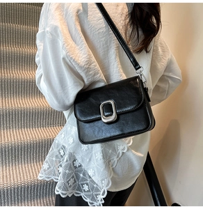 Detailed view of black textured leather crossbody bag with silver rectangular metal buckle