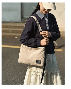Detailed view of beige crossbody bag with adjustable black strap and woven label