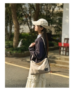 Detail of a beige minimalist crossbody tote bag with brand label in a casual outdoor setting