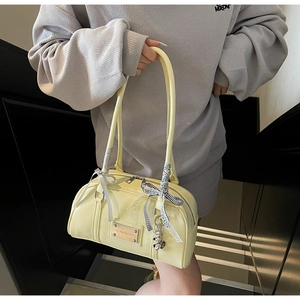 Detail of light yellow patent leather shoulder bag with chic ribbon and brand nameplate