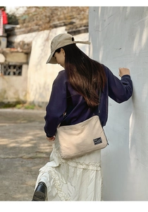 Outdoor shot of a beige canvas tote bag with a small black square logo patch on the side
