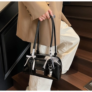 Detail of black glossy shoulder bag with bow accents and silver heart charm on stairs