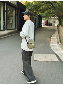 Outdoor street shot of an olive green canvas square crossbody bag with black straps