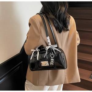 Detail of black glossy shoulder bag with bow and heart charm on a stylish model