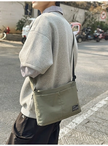 Detail of olive green nylon crossbody bag with dual compartments and logo patch in street scene
