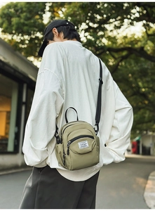 Detail showing an olive green nylon shell bag worn by a model in a casual street setting