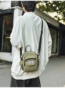 Olive green nylon crossbody bag detail showing front zipper pocket and logo patch