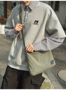 Detailed view of an olive green nylon crossbody bag paired with a casual polo sweatshirt