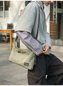 Detail of light olive green nylon crossbody bag with square brand label and stitching