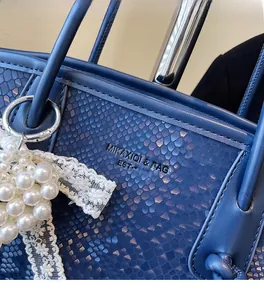 Detail of navy snake-textured leather handbag featuring pearl and lace charms