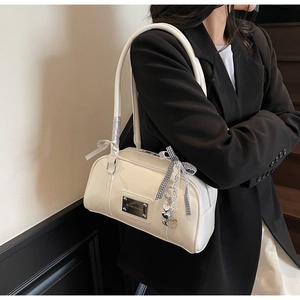 Detail of cream white shoulder bag with decorative bow and heart pendant on a black blazer