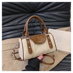 Detail der beige gewebten Boston-Tasche mit braunem Ledergriff und silbernen Nieten