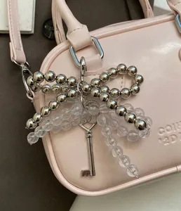 Close-up of beaded bow charm with vintage key pendant on a pink leather handbag