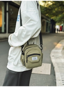 Detailed shot of an olive green nylon crossbody bag with a white woven label and black strap