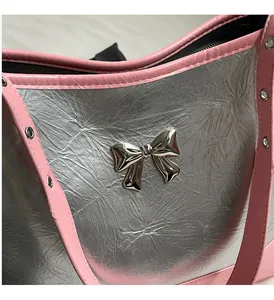 Detail of silver metallic underarm bag with pink strap and shiny bow hardware