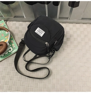 Detail view of a black nylon crossbody bag with an adjustable strap and white logo label