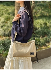 Detail of khaki nylon crossbody bag with dual front pockets and woven design label