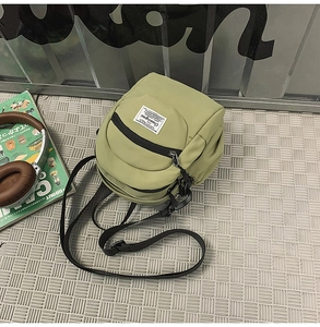 Flat lay of an olive green nylon crossbody bag with black zipper pocket and shoulder strap