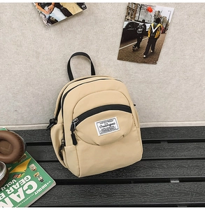 Detail of a beige nylon mini square bag with black zipper and woven label on a wooden bench