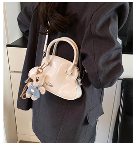 Bolso de concha blanco crema con colgante de oso, llevado como bandolera sobre blazer