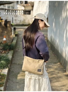 Detail of khaki canvas tote bag with a small black brand patch and adjustable strap