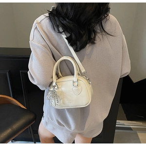 Detail of cream white crossbody pillow bag with heart handles and silver bow charm accessory