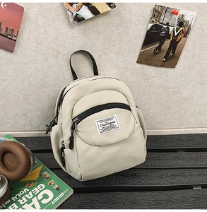 Detail of a minimalist beige mini backpack with a square fabric label on the front pocket