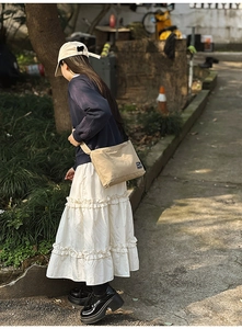 Khaki nylon shoulder bag with small logo tag shown on a model in a natural outdoor setting