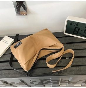 Detail of khaki nylon crossbody bag showing the zipper and brand label on a bench