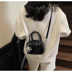 Detail of a shiny black patent leather crossbody pillow bag with silver bow charm on model