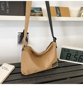 Detail view of khaki nylon tote bag with dual shoulder straps on a wooden stool