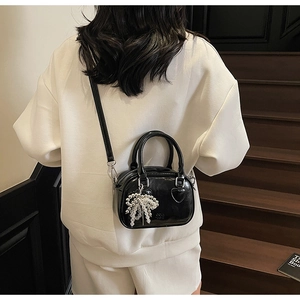Detail of black glossy handbag with pearl bow charm and elegant heart embossing