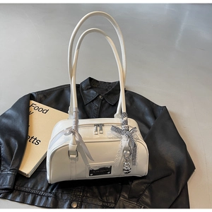 Detail of white glossy underarm bag with decorative ribbons and lace bear charm on black jacket