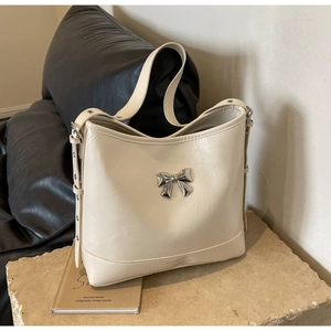 Close-up of cream textured leather shoulder bag featuring a silver metal bow detail