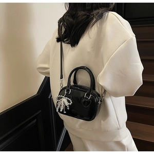 Detail of black glossy mini pillow bag with heart patch and pearl charm on a model