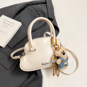 Detalle de bolso color crema en forma de concha con un llavero de oso de peluche