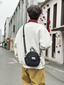 Black nylon mini crossbody bag with rectangular label and adjustable strap shown on model