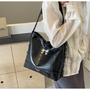 Detail of black faux leather tote with vintage texture and silver metal bow ornament